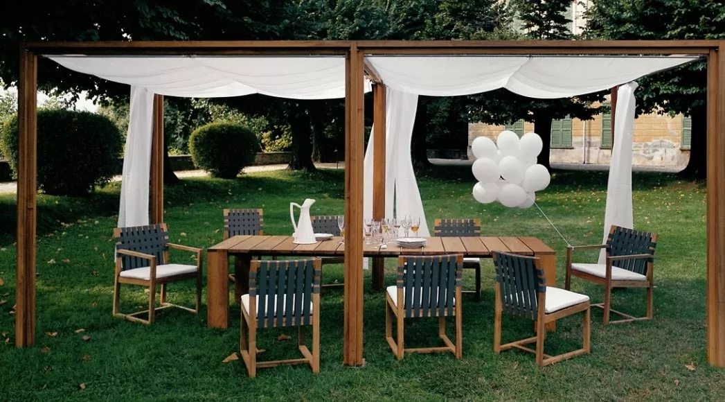 Roda Essgruppe in einem Garten mit Holztisch, acht Stühlen mit dunklen Geflecht und weißem Stoffdach, umgeben von grüner Natur.