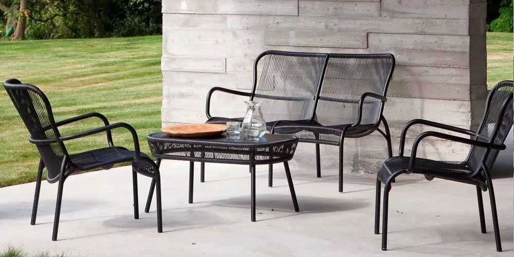 Vincent Sheppard Loop Gartenmöbel-Set in Schwarz auf einer Terrasse mit Betonwand und Rasen im Hintergrund.