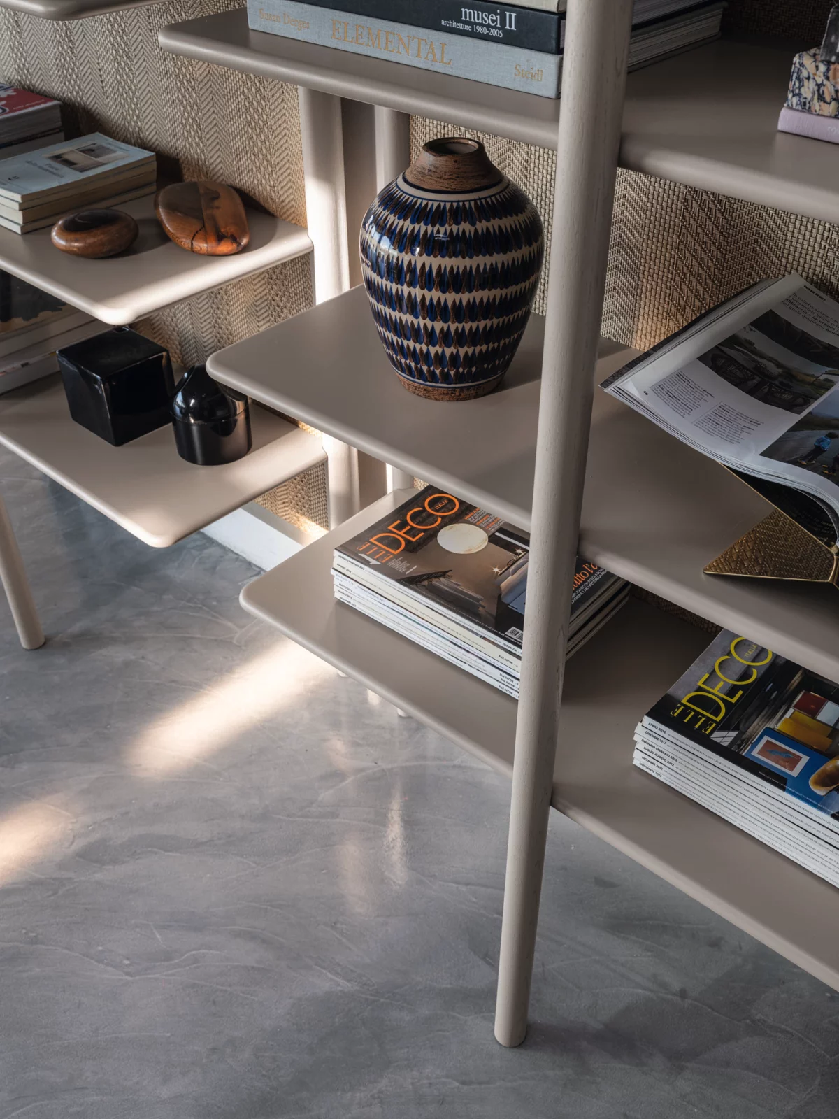 Ein Regal mit Büchern Zeitschriften und Dekorationsgegenständen wie einer Vase und Holzobjekten in einem modernen Wohnzimmer.