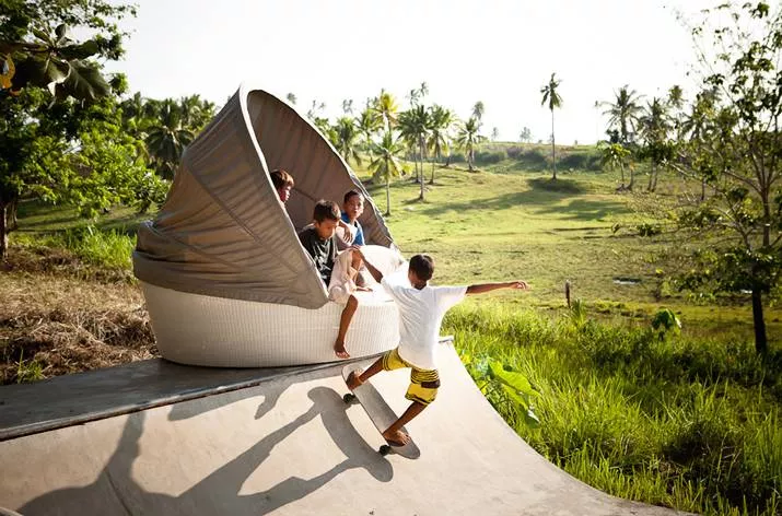 Kinder spielen auf einer Dedon Orbit Sofainsel im Freien in einer grünen Landschaft mit Palmen im Hintergrund.