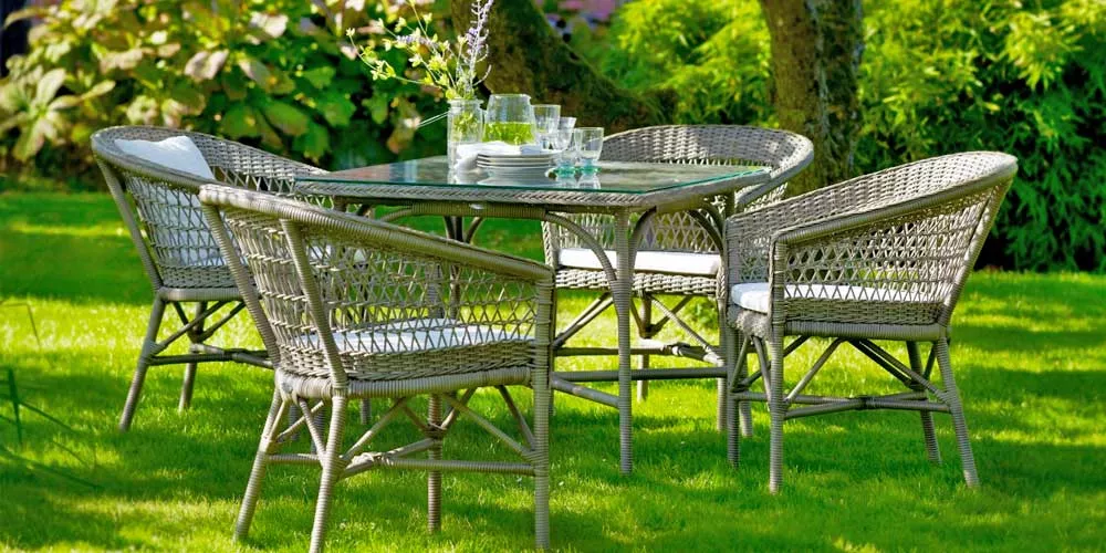 Sika-Design Emma Essgruppe aus Rattan in Naturfarbe auf grünem Rasen im Garten, bestehend aus rundem Tisch und vier Stühlen.