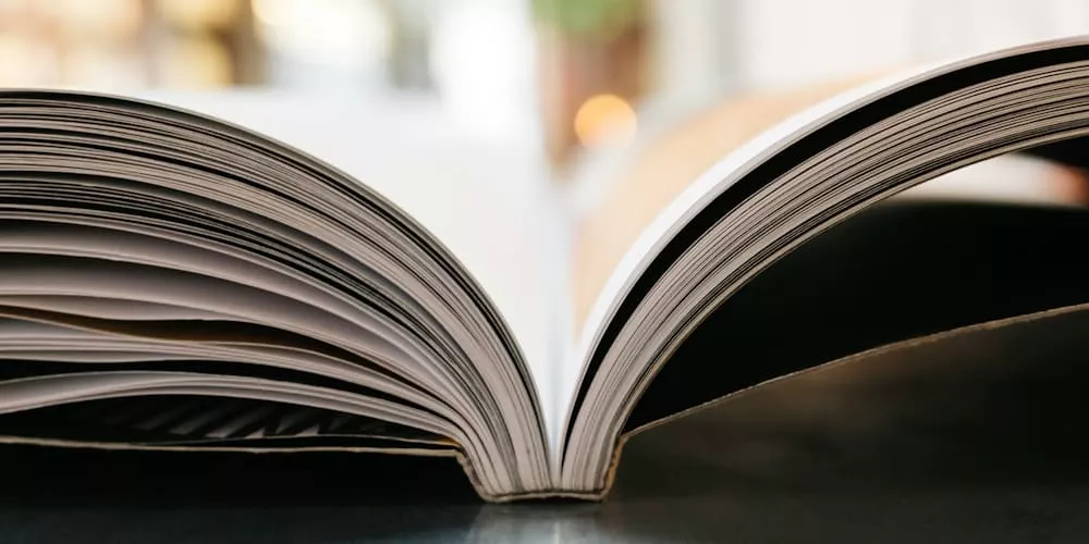 Offenes Buch auf einem Holztisch, Seiten leicht gebogen, mit unscharfem Hintergrund, stimmungsvolles Bild.