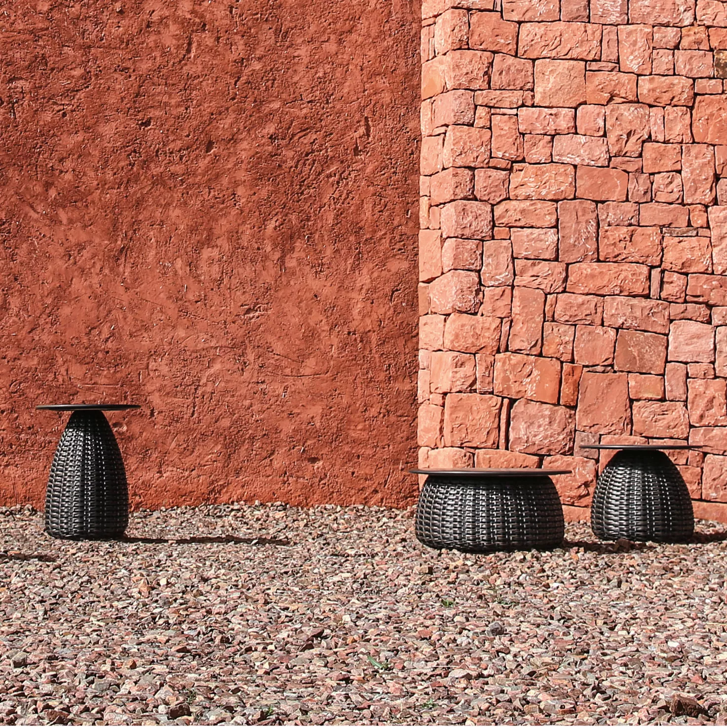 Dedon Porcini Beistelltisch in verschiedenen Größen vor einer roten Steinmauer auf einem Kiesboden