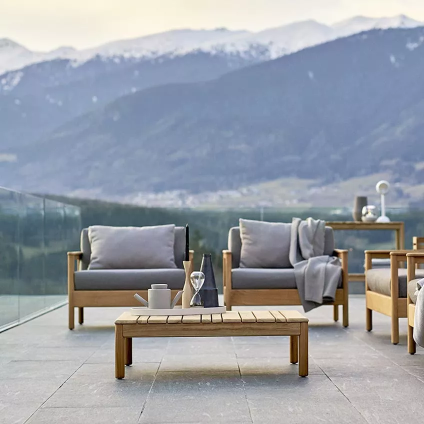 Varaschin Bali Loungesessel mit Teakholzgestell in Grau auf einer Terrasse mit Bergblick bei Sonnenuntergang.