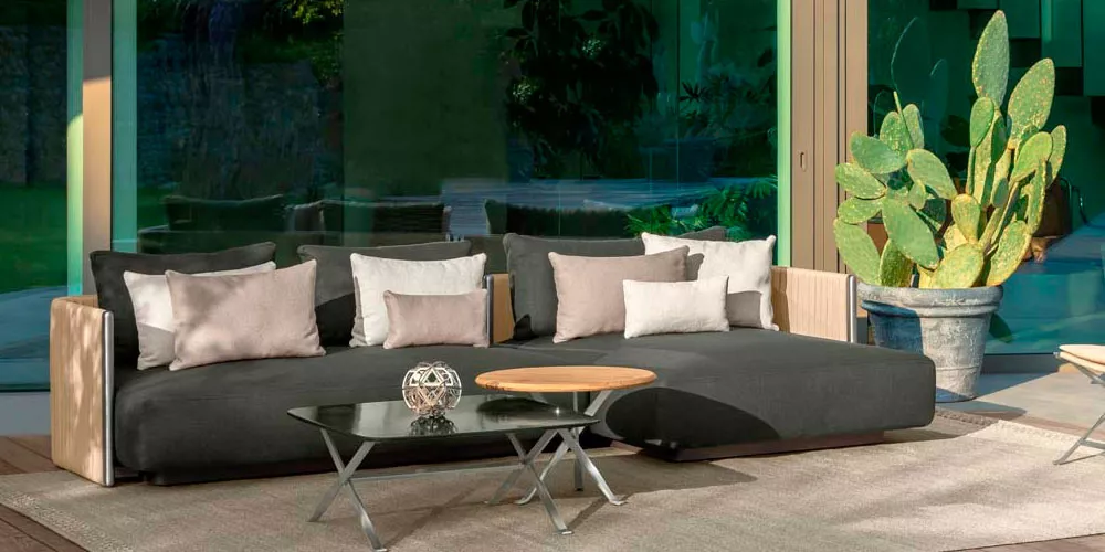 Talenti George Loungegruppe in Anthrazit auf einer Terrasse mit Glaswand und Kaktus im Hintergrund, stimmungsvolle Gartenmöbel-Präsentation.