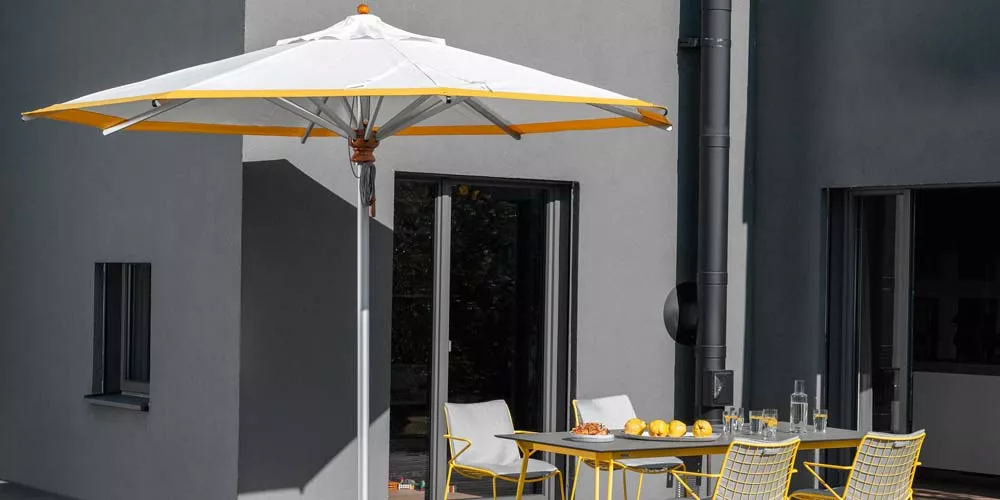 Weishäupl Alu-Sonnenschirm in Weiß und Gelb auf einer modernen Terrasse vor einem grauen Gebäude.