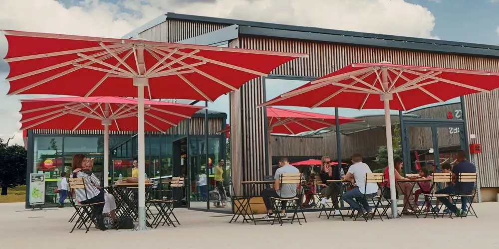 Rote May Sonnenschirme Albatros über einem Café im Freien, moderne Architektur im Hintergrund, entspannte Atmosphäre.