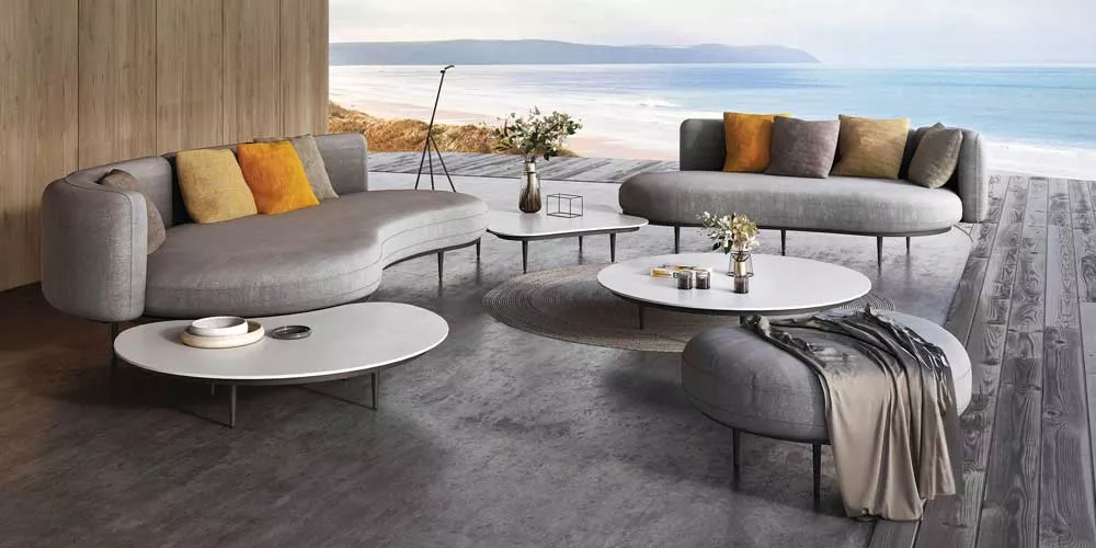 Royal Botania Organix Loungegruppe in Grau auf Holzterrasse mit Meerblick, bestehend aus Sofas und Tischen, stimmungsvolle Outdoor-Szene.