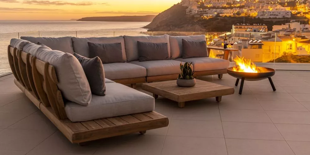 Alexander Rose Sorrento Lounge-Set in Holzoptik auf einer Terrasse mit Meerblick bei Sonnenuntergang, gemütliche Stimmung.