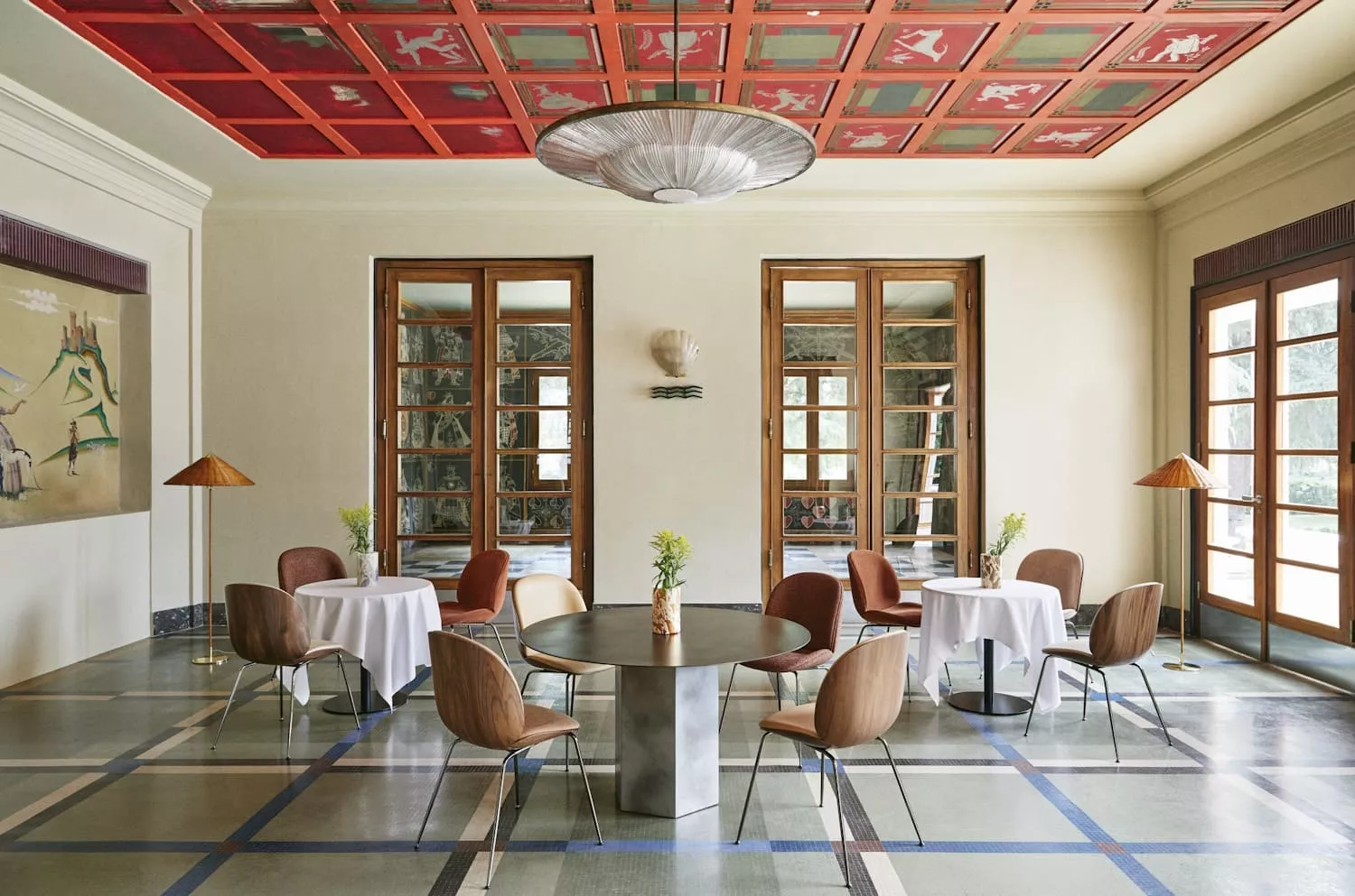 Ein stilvoll eingerichteter Raum mit Gubi Stühlen und Tischen in einem eleganten Ambiente mit kunstvoll bemalter Decke und großen Fenstern