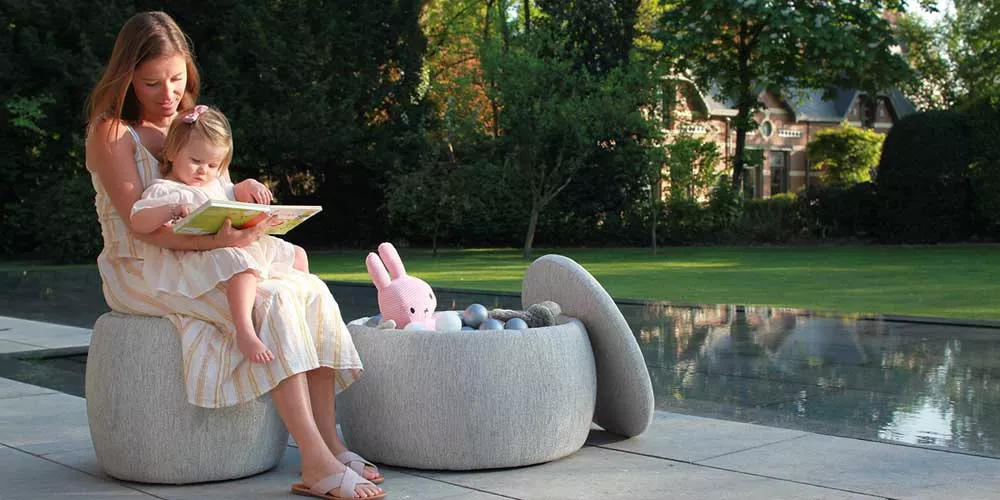 Frau und Kind sitzen auf der grauen Royal Botania Tono Loungegruppe im Garten, umgeben von grüner Natur und einem Pool im Hintergrund.