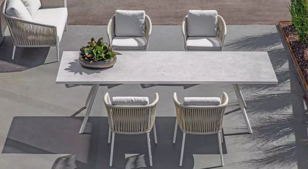 Fischer Möbel Cosmo Essgruppe in Weiß auf einer Terrasse, bestehend aus einem langen Tisch und vier Stühlen mit Kissen, aus der Vogelperspektive.