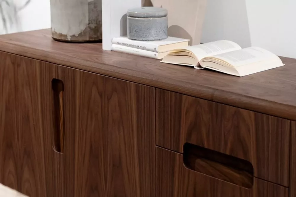 RIVA1920 Sideboard in dunklem Holz, Detailansicht mit Büchern und Dekoration auf der Oberfläche, vor weißer Wand.