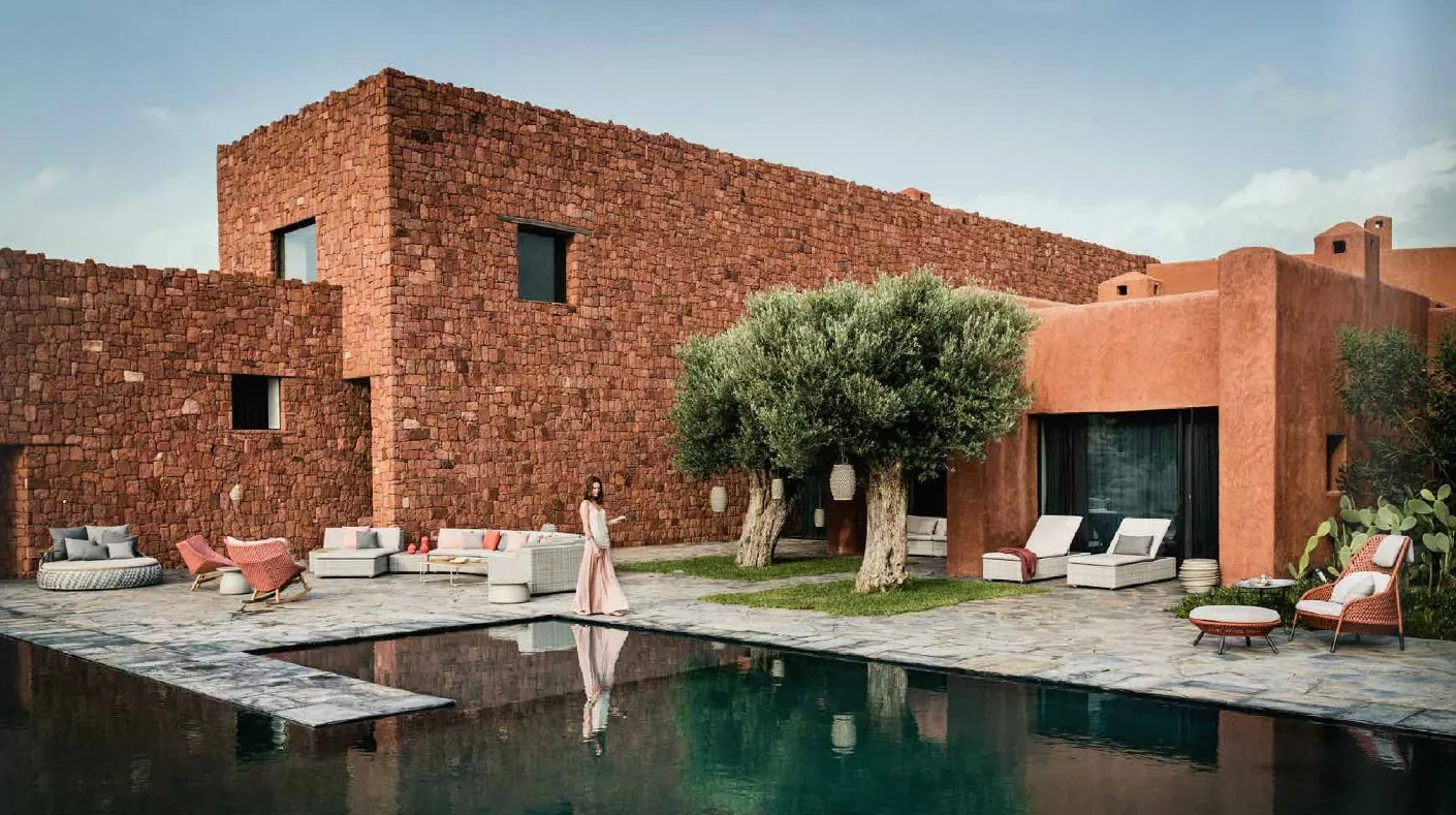 Eine Frau steht am Pool vor einem modernen Haus mit Dedon Mbrace Lounge Möbeln im Garten und genießt die entspannte Atmosphäre