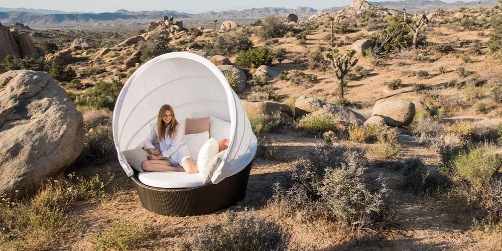 Eine Frau entspannt sich in einem Dedon Orbit Loungesessel in einer Wüstenlandschaft umgeben von Felsen und Sträuchern.