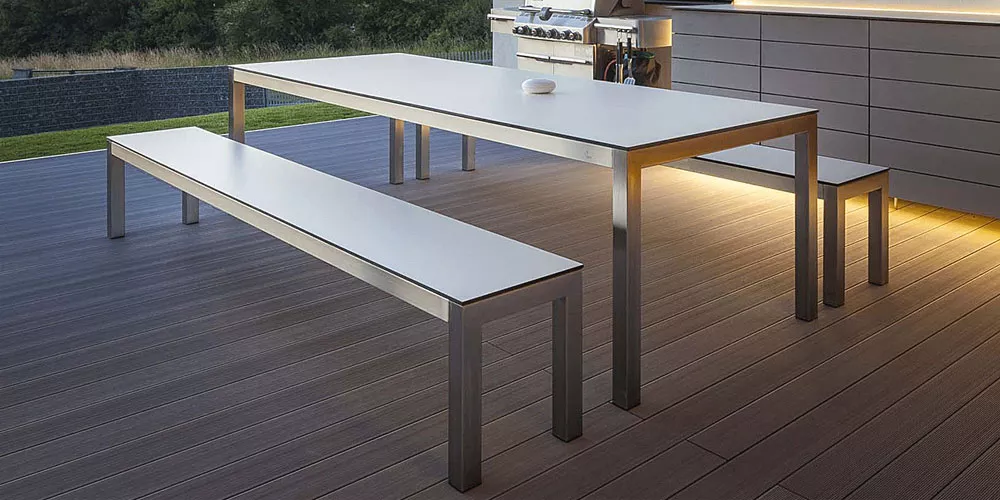 Todus Leuven Kollektion, weißer Tisch und Bänke aus Metall, auf moderner Terrasse bei Dämmerung, stimmungsvolle Beleuchtung.