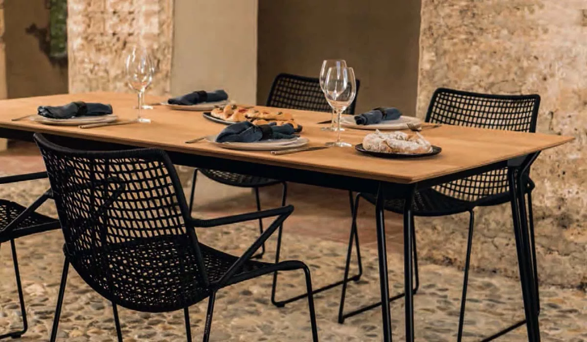 Weißhäupl Tisch in Holzoptik mit schwarzem Metallgestell, gedeckt mit Geschirr und Gläsern, auf einem rustikalen Steinboden.