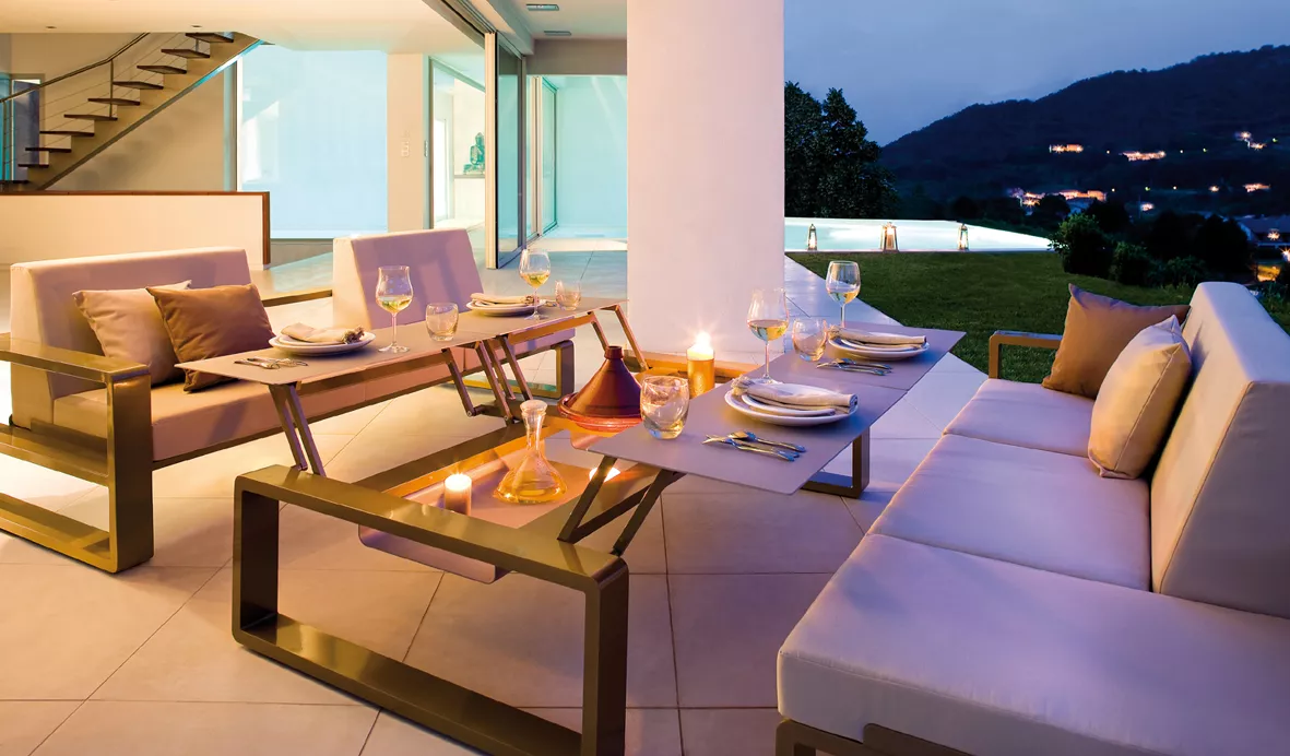 Variabler Tisch Quattro Kama von Ego, in modernem Design, auf einer Terrasse bei Abenddämmerung, gedeckt mit Geschirr und Kerzen.