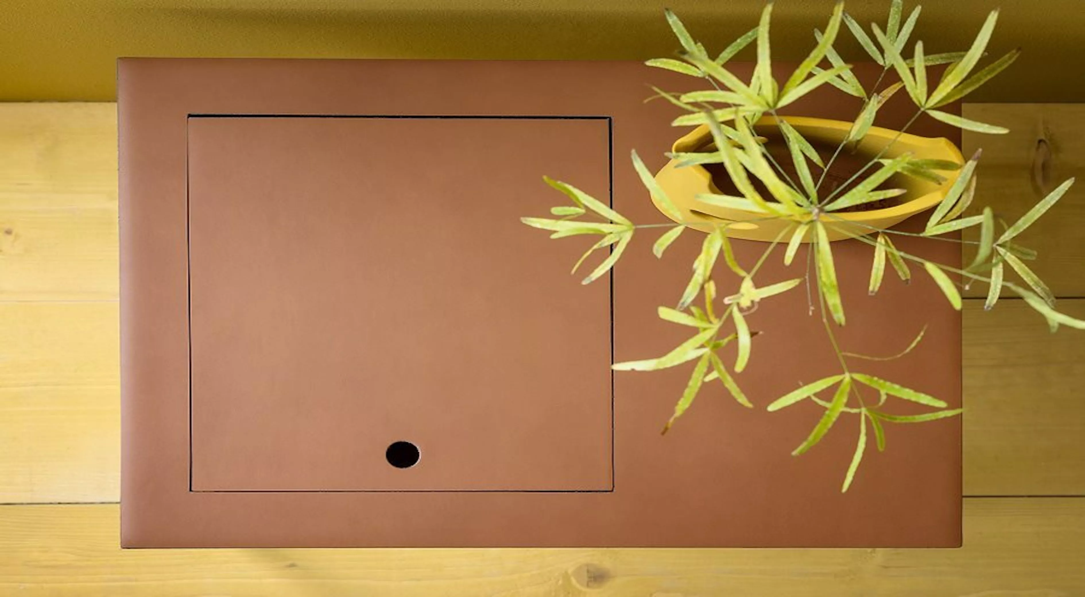 Braunlederne Taschino 643 von Villa Schmidt, quadratisch, auf Holztisch mit Pflanze, aus der Vogelperspektive fotografiert.