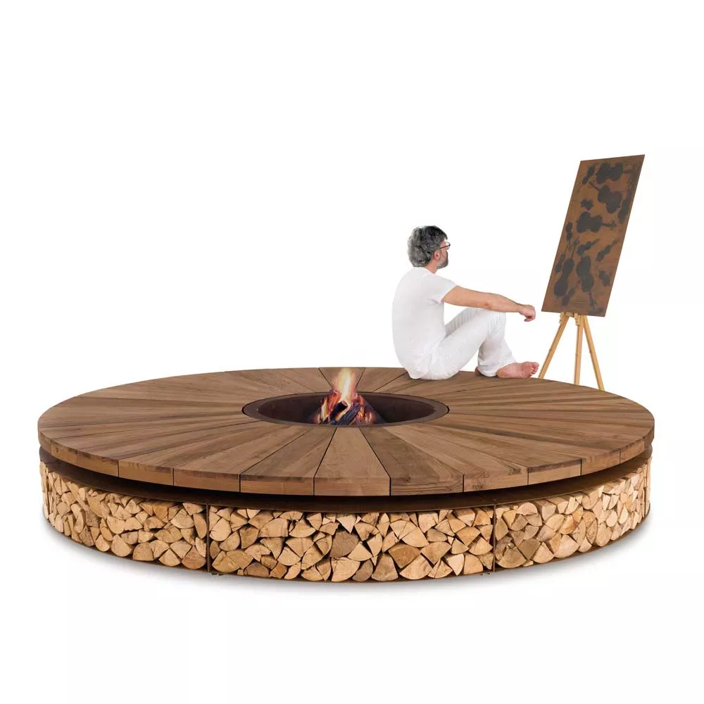 Ein Mann sitzt auf dem Boden und malt auf einer Leinwand neben der AK47 Art Kastanienholz Stahl Feuerstelle 300 cm in einem hellen Raum