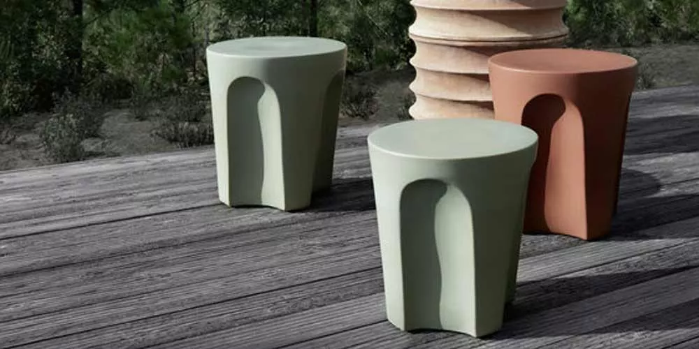 Drei BeB Italia Colosseo Hocker in grün und terrakotta stehen auf einer Holzterrasse im Freien umgeben von Bäumen und Pflanzen.