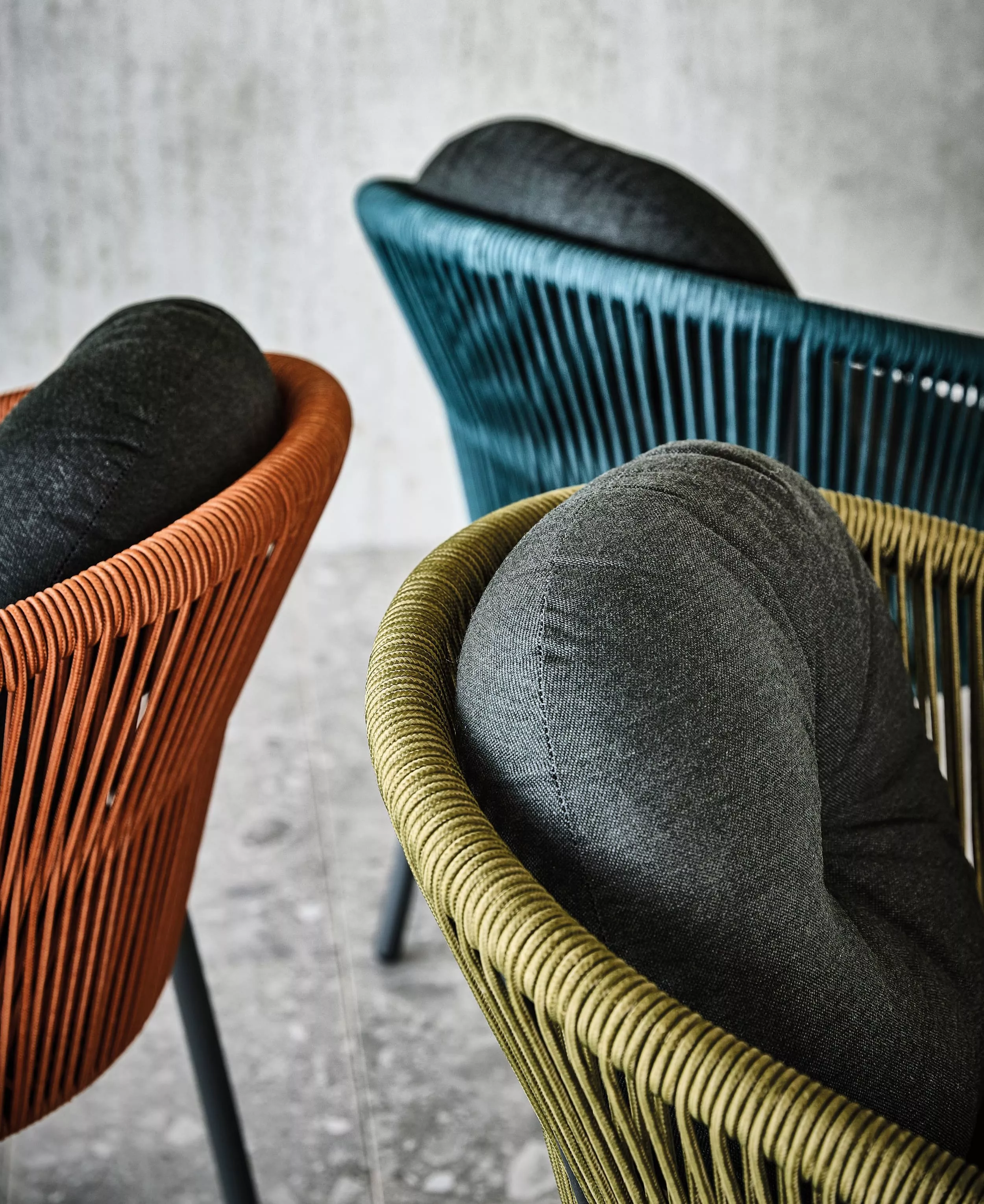 Drei Solpuri Loop-A Stühle in verschiedenen Farben mit grauen Kissen in einer modernen Umgebung.