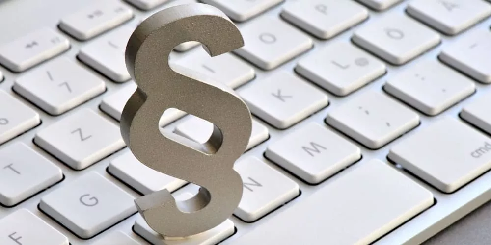 Silbernes Paragraphenzeichen steht auf einer weißen Computertastatur, symbolisiert rechtliche Themen im digitalen Kontext.