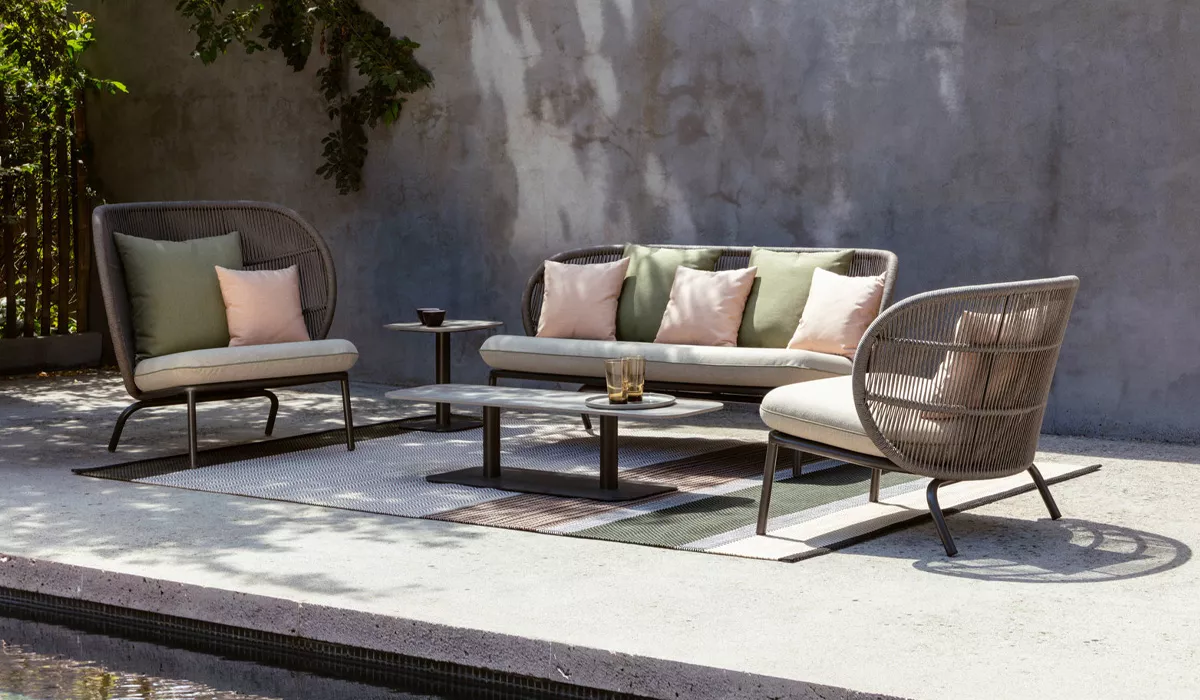 Vincent Sheppard Loungemöbel in Grau und Beige auf einer Terrasse mit Betonwand im Hintergrund, stimmungsvolles Outdoor-Setting.