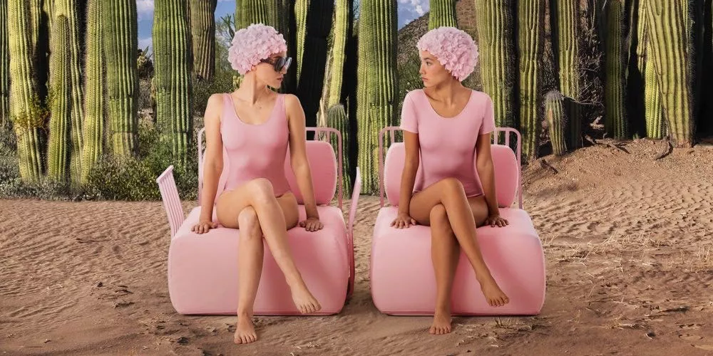 Zwei Frauen in rosa Badeanzügen und Badekappen sitzen auf rosa Diabla-Sesseln vor einer Wüstenlandschaft mit Kakteen.