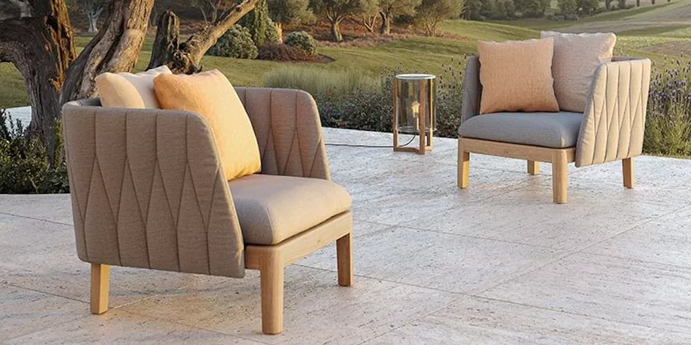 Zwei beige-graue Outdoor-Sessel von Villa Schmidt auf einer Terrasse mit Blick auf eine grüne Landschaft bei Sonnenuntergang.