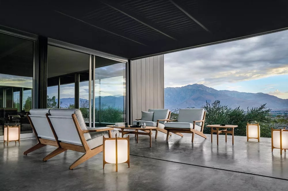 Gloster Bay Gartenmöbel-Set in hellem Grau auf einer Terrasse mit Bergblick, bestehend aus Sofas, Sesseln und Tischen, umgeben von Laternen.