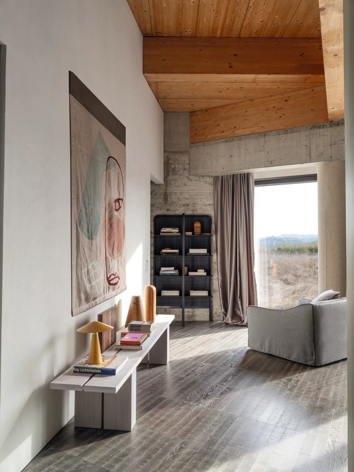 Ein modernes Wohnzimmer mit Gervasoni Sofa und Kunstwerk an der Wand ein Regal mit Körben und ein Fenster mit Blick auf die Landschaft