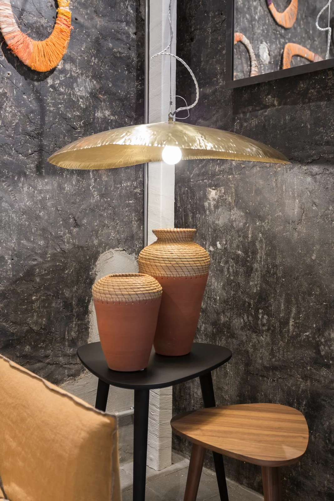 Gervasoni Via Durini Lampe beleuchtet eine Szene mit zwei dekorativen Vasen auf einem Tisch vor einer rustikalen Wand in einem stilvollen Raum.