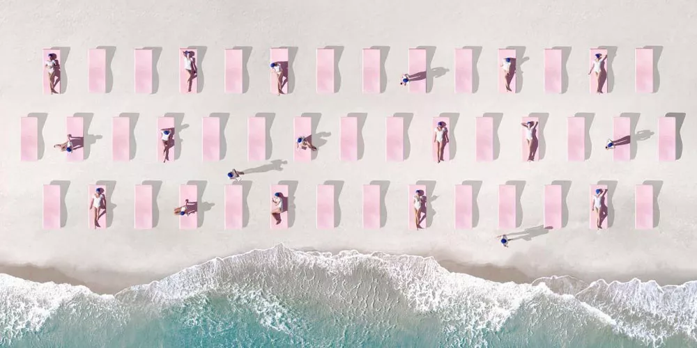 Luftaufnahme von rosa Diabla Strandliegen in Reih und Glied am Sandstrand mit Wellen im Vordergrund.