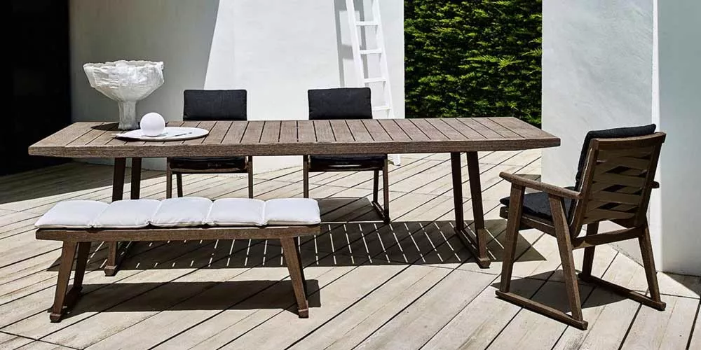 Essgruppe von B&B Italia Gio bestehend aus einem Holztisch mit Stühlen und einer Bank auf einer Terrasse bei Tageslicht.
