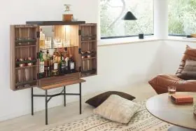 Barschrank HARRI von Peter Fehrentz in Holzoptik mit schwarzem Rahmen, geöffnet in modernem Wohnzimmer mit Tageslicht und Pflanzen im Hintergrund.