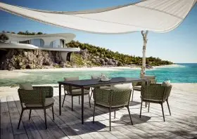 DEDON BELLMONDE Essgruppe auf einer Terrasse mit Meerblick und moderner Architektur im Hintergrund