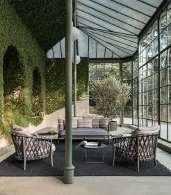 B&B Italia Erica 19 Outdoor Lounge in einem stilvollen Wintergarten mit Glaswänden und grüner Hecke im Hintergrund