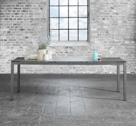 Solpuri Classic Alu Tisch in einem industriellen Ambiente mit einer Pflanze und einer Flasche auf der Tischplatte vor einer Backsteinwand und einem Fenster