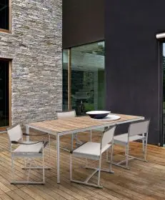 B&B Italia Mirto Outdoor Essgruppe auf einer Holzterrasse vor einem modernen Haus mit Stein- und Glasfassade und einer Schale auf dem Tisch