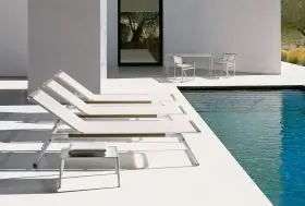 Drei B&B Italia Mirto Outdoor Liegestühle und ein Beistelltisch stehen neben einem Pool in einer modernen Außenumgebung.