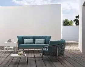 B&B Italia Erica Loungegruppe bestehend aus einem Sofa einem Sessel und zwei Tischen auf einer Terrasse mit Holzboden und weißer Wand im Hintergrund