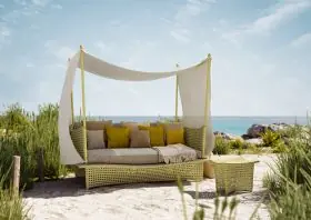 DEDON DAYDREAM Loungeinsel mit Kissen und Decke steht am Strand unter blauem Himmel und lädt zum Entspannen ein