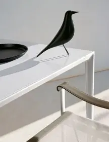 B&B Italia Mirto Outdoor Essgruppe mit weißem Tisch und beigem Stuhl auf einer Terrasse mit einer schwarzen Vogelskulptur auf dem Tisch