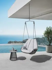 Solpuri Chill-A Hängesessel in modernem Design auf einer Terrasse mit Meerblick und einem Beistelltisch mit Dekorationen Moodbild