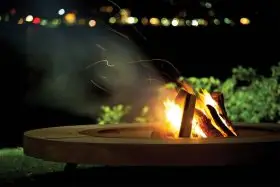 AK47 Rondo Feuerstelle aus Santafiora Trachyt und Stahl 206 cm im Freien bei Nacht mit brennendem Feuer und Funken im Hintergrund