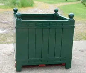 Orangerie Pflanzkübel aus lackiertem Akazienholz steht auf einer Palette im Freien auf einem Betonboden mit Gras im Hintergrund