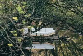 Calma Alat Wood Loungesofa in Weiß, 350 cm, auf einer Insel inmitten eines ruhigen, bewaldeten Flussufers platziert.