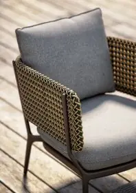 DEDON BELLMONDE Sessel mit grauem Kissen und geflochtenen Armlehnen auf einer Holzterrasse in der Sonne