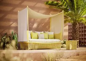 DEDON DAYDREAM Lounge im Freien mit gelbem Geflecht und weißen Kissen unter einem Sonnendach umgeben von Palmen und Kakteen in einer Wüstenlandschaft